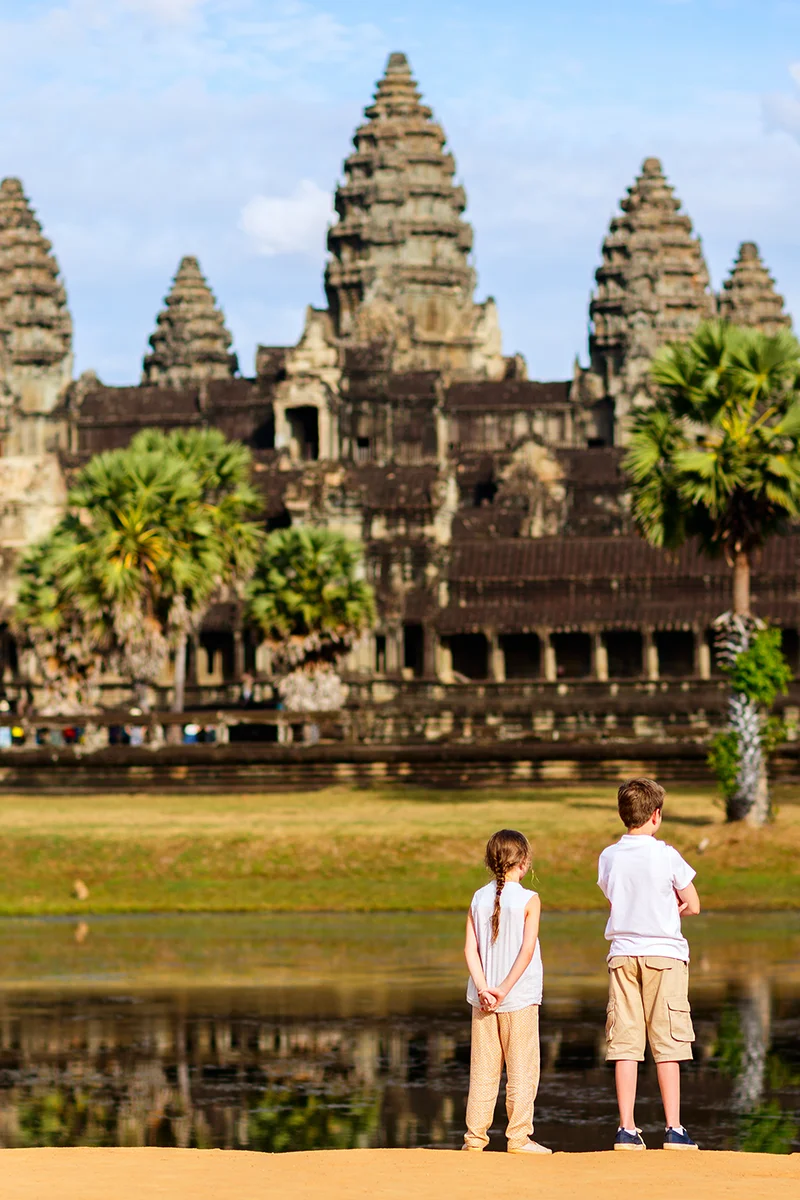 Two children looking at the iconic reflection of Angkor Wat temple during golden sunset hour