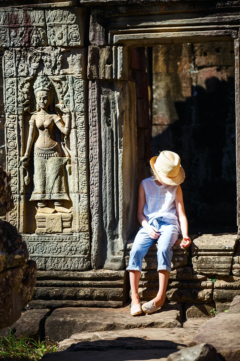 Child exploring Banteay Kdei temple in Angkor with stunning ancient carvings visible on the wall