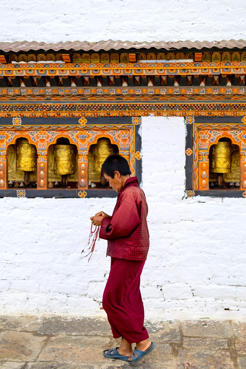 Bhutanese woman walking past ornate temple wall with prayer wheels