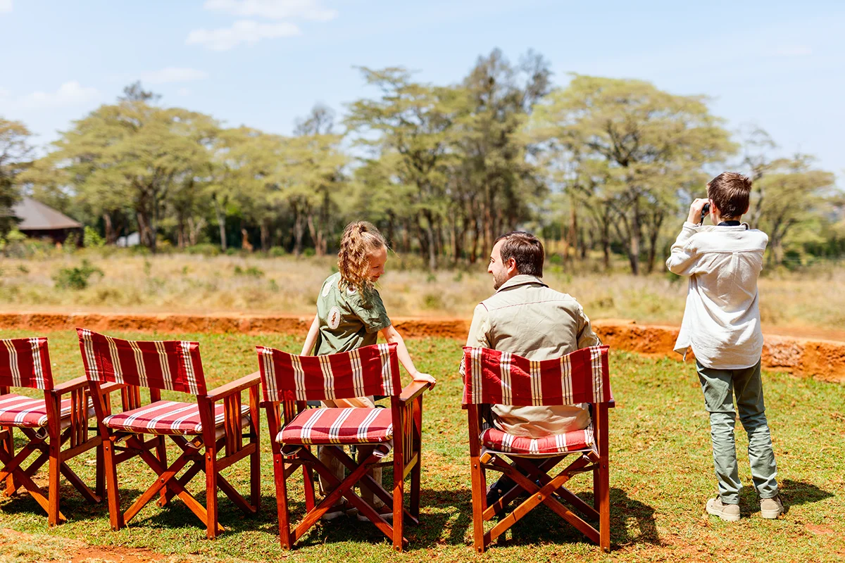 Father and two children on the outdoor terrace of Giraffe Manor in Kenya watching giraffes roaming in the distance