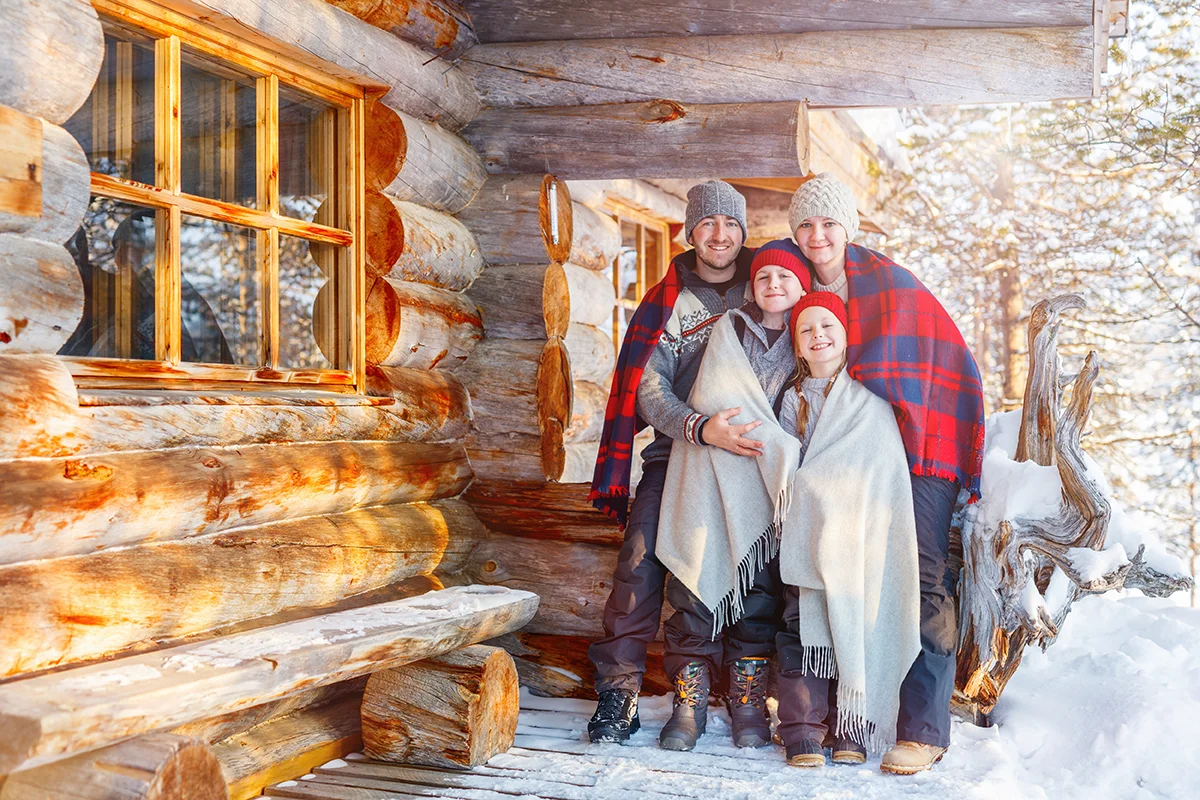 Family on vacation posing outside their log cabin at Kakslauttanen Arctic Resort in Finland
