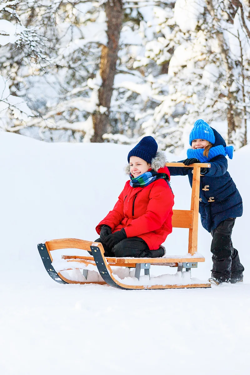 Children playing with wooden sled in the snowy grounds of Kakslauttanen Arctic Resort in Finland