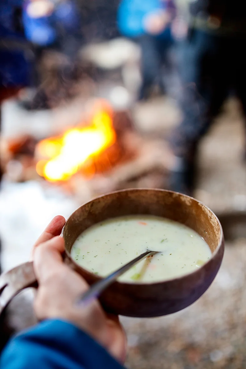 Traditional Finnish salmon soup served in mug by a campfire in snow-covered Lapland