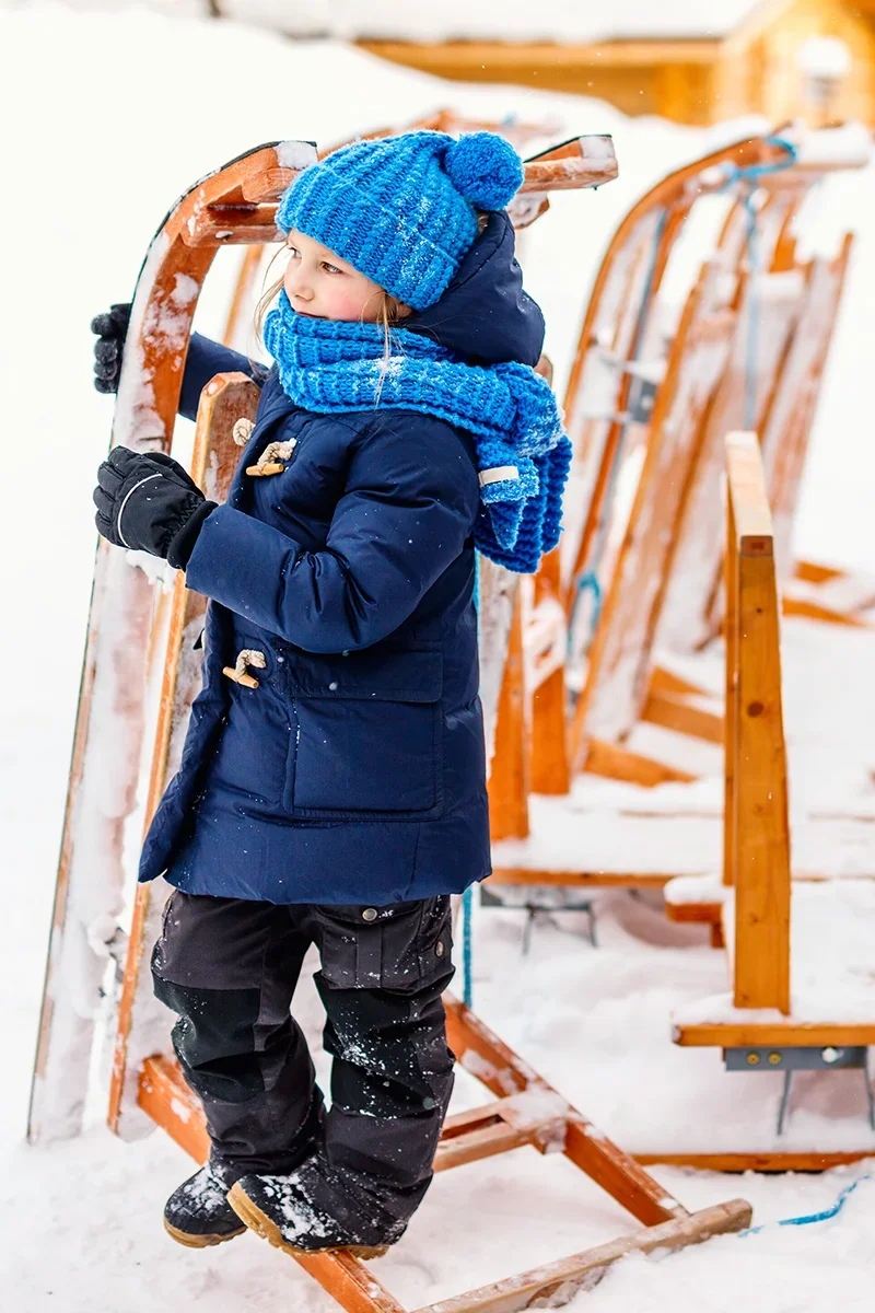 Child with a wooden sled in the snowy grounds of Kakslauttanen Arctic Resort in Finland