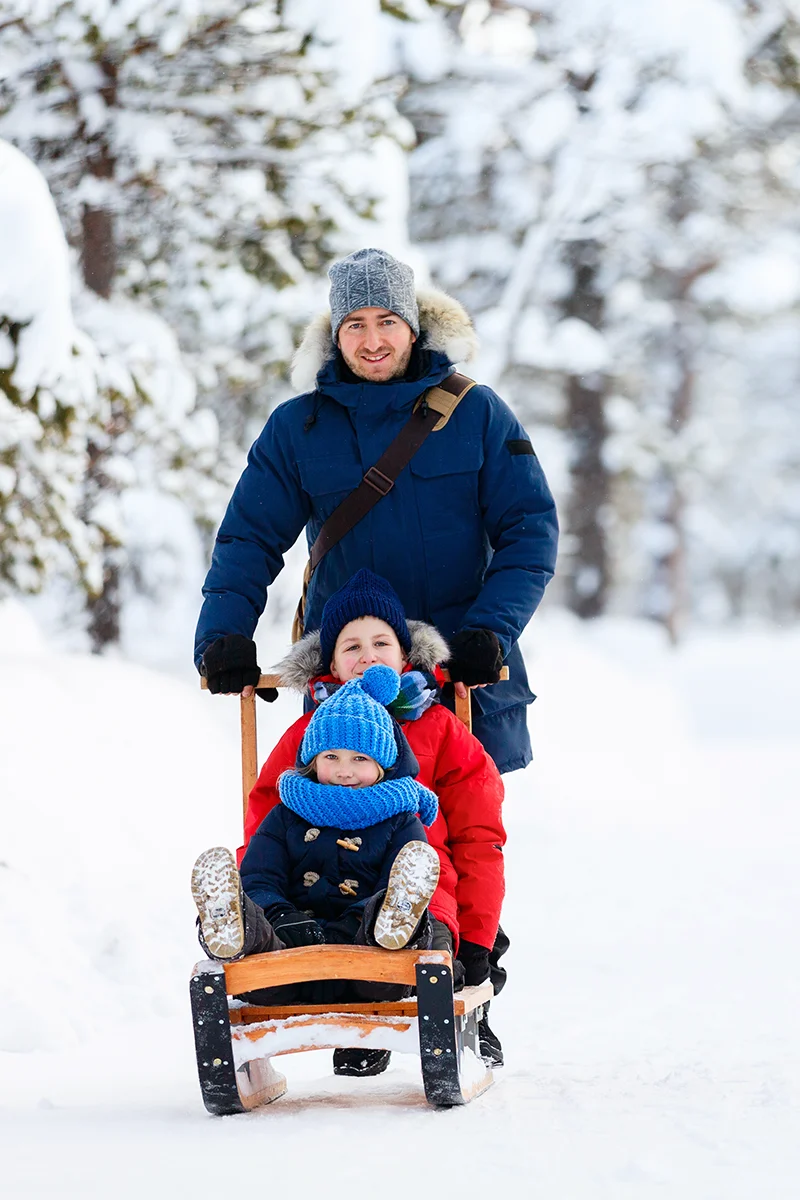 Family playing with wooden sled in the snow at Kakslauttanen Arctic Resort in Finland