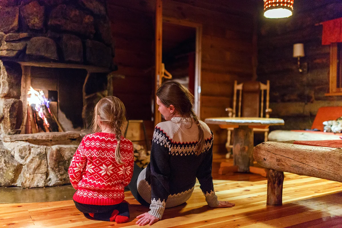Family enjoying cozy evening by a fireplace at log cabin in Kakslauttanen Arctic Resort in Finland