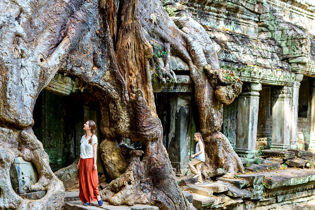 Mother and child exploring Preah Khan temple in Angkor where giant tree roots creeping over the ruins