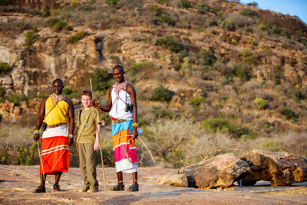 Child walking with Samburu warriors in traditional attire during a guided safari walk in Kenya