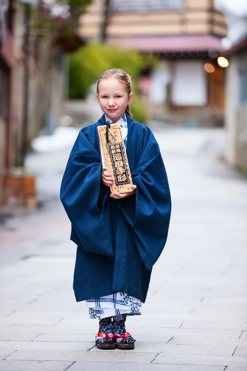 Child wearing traditional Japanese attire holding key to public baths in Shibu Onsen